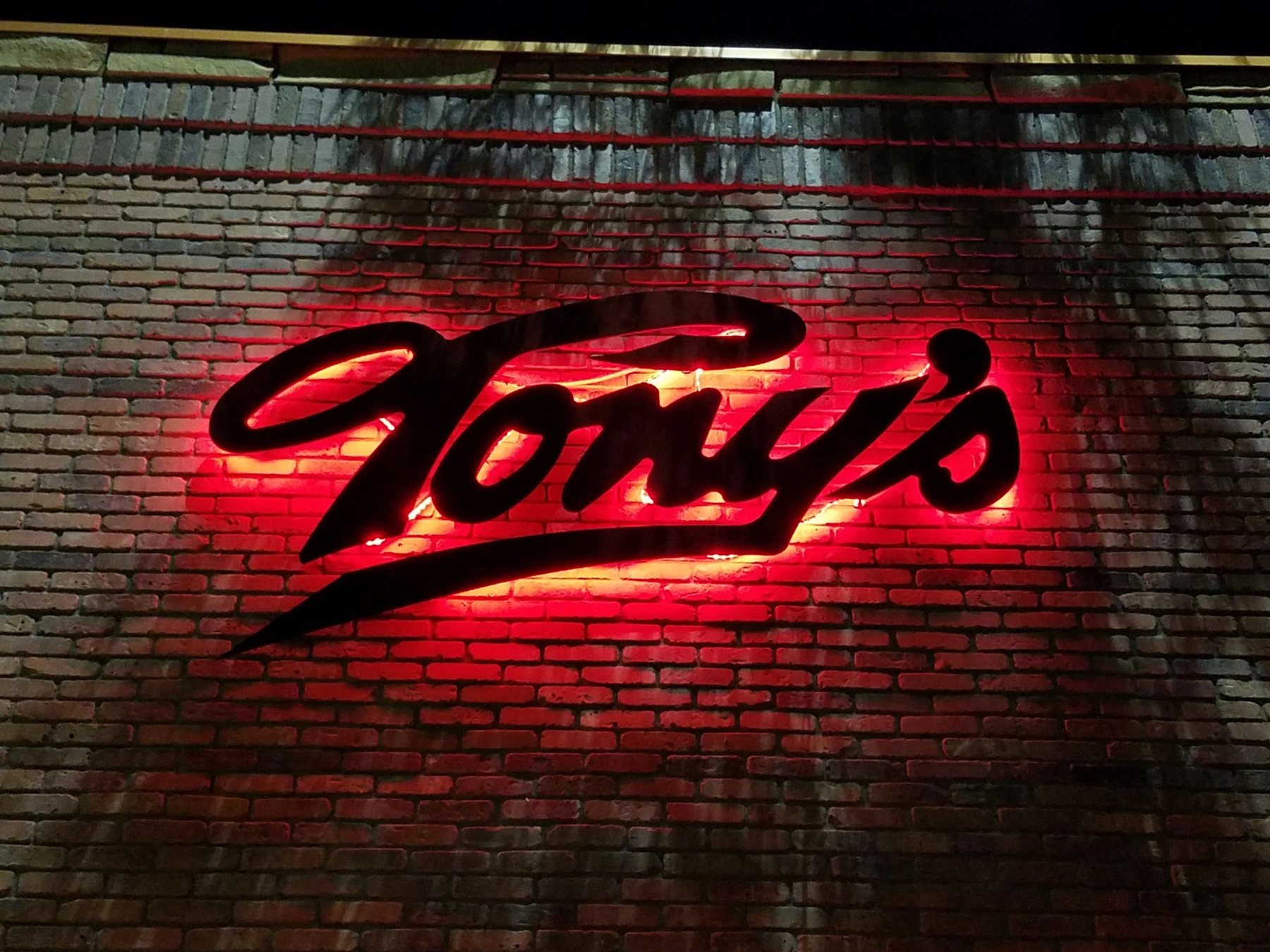 The red neon Tony's script glowing on the brick